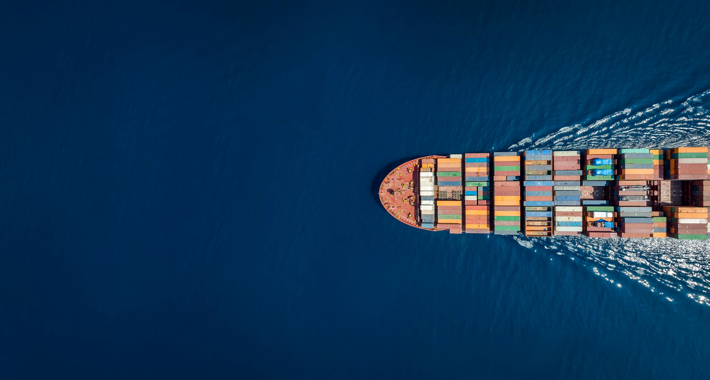 Shipping vessel carrying containers travelling out at sea.